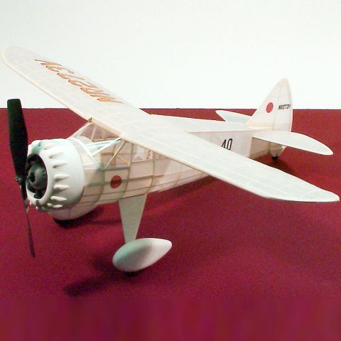 Detailansicht eines Dumas Gummimotorflugzeugs mit Propeller, auf rotem Untergrund. Modell zeigt filigrane Bauweise und charakteristische Merkmale des Flugzeugs. Ideal für Modellbau-Enthusiasten.